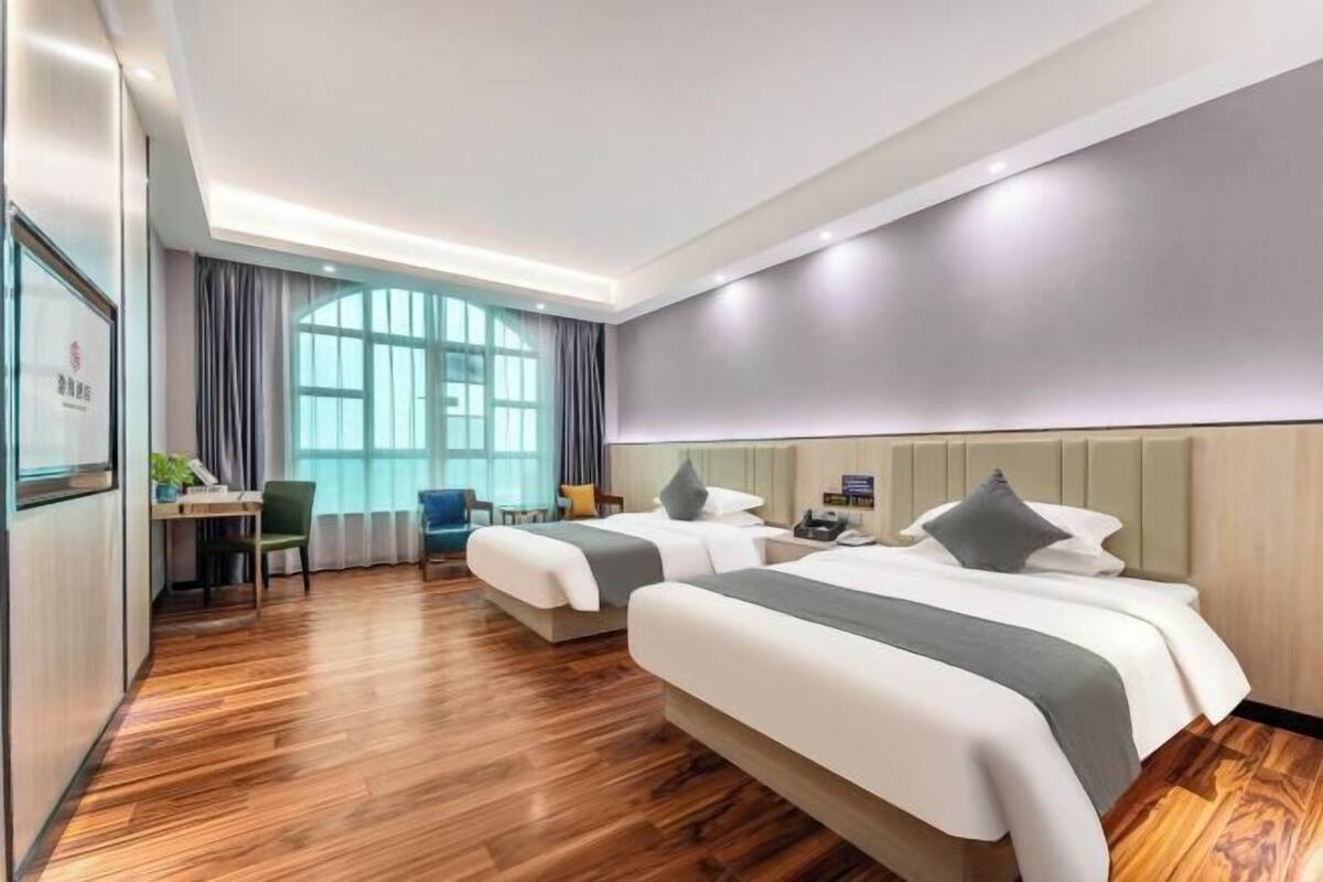 A hotel room with two beds, a desk, a chair, and a large window.