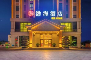 Un hotel con una entrada destacada, un cartel con caracteres chinos y una fachada bien iluminada.