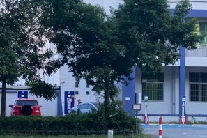 A parking area with cars, a building with blue and white exterior, and trees. - Bohai Hotel （Taishan Chonglou) (Taishan)
