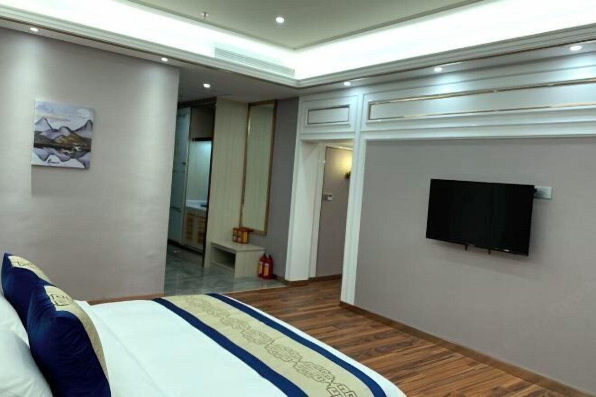 A hotel room with a bed, a television mounted on the wall, and a wooden floor.
