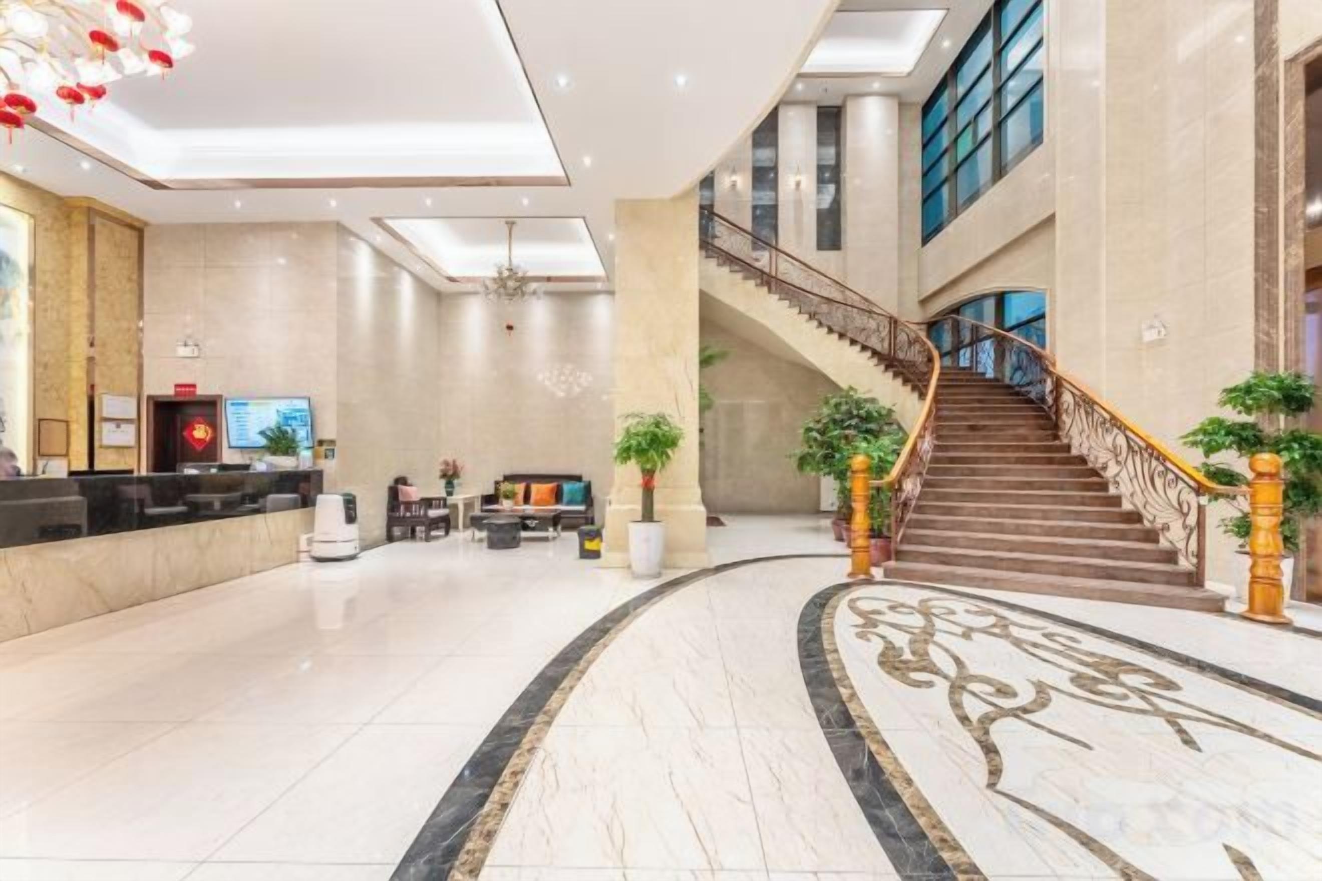 A hotel lobby with a reception desk, seating area, and a staircase.