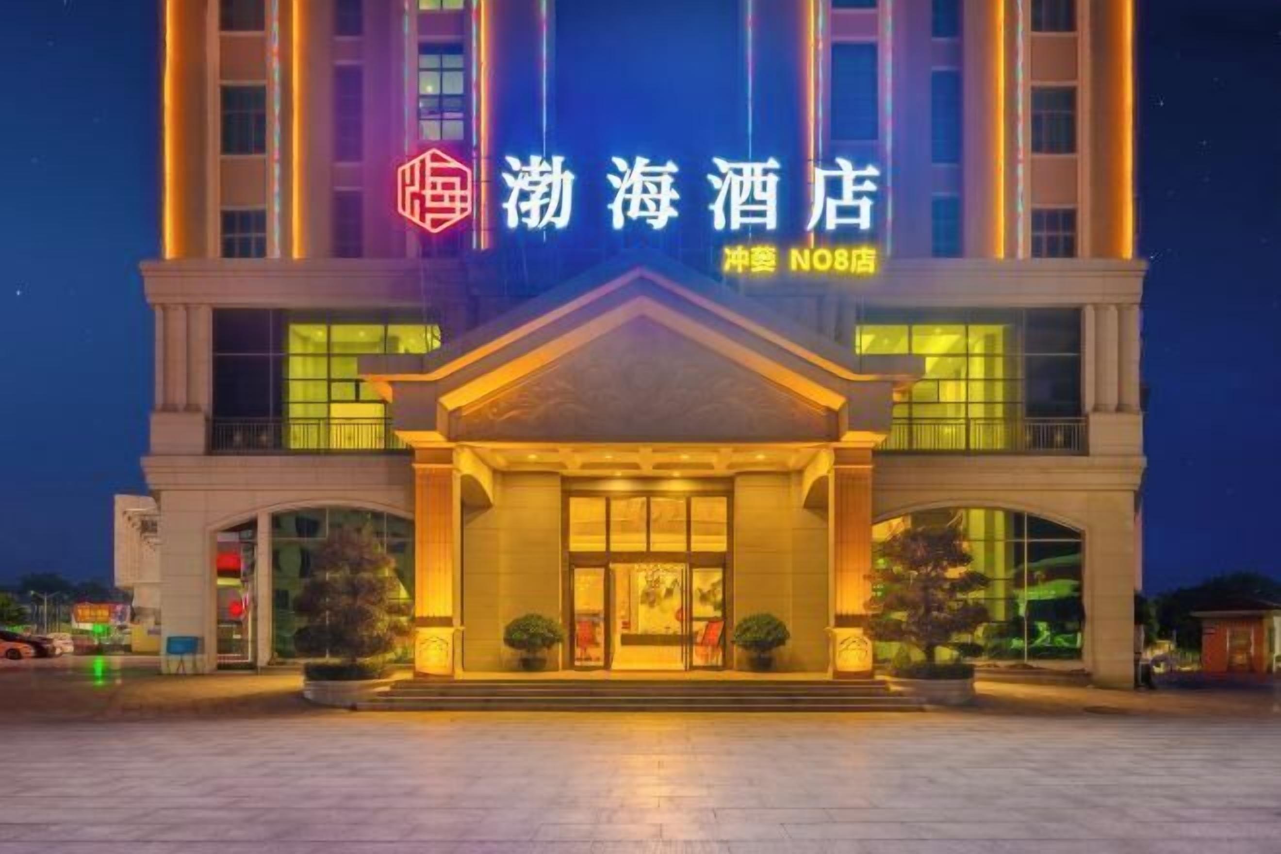 A hotel entrance with a prominent sign, a covered entrance area, and potted plants.