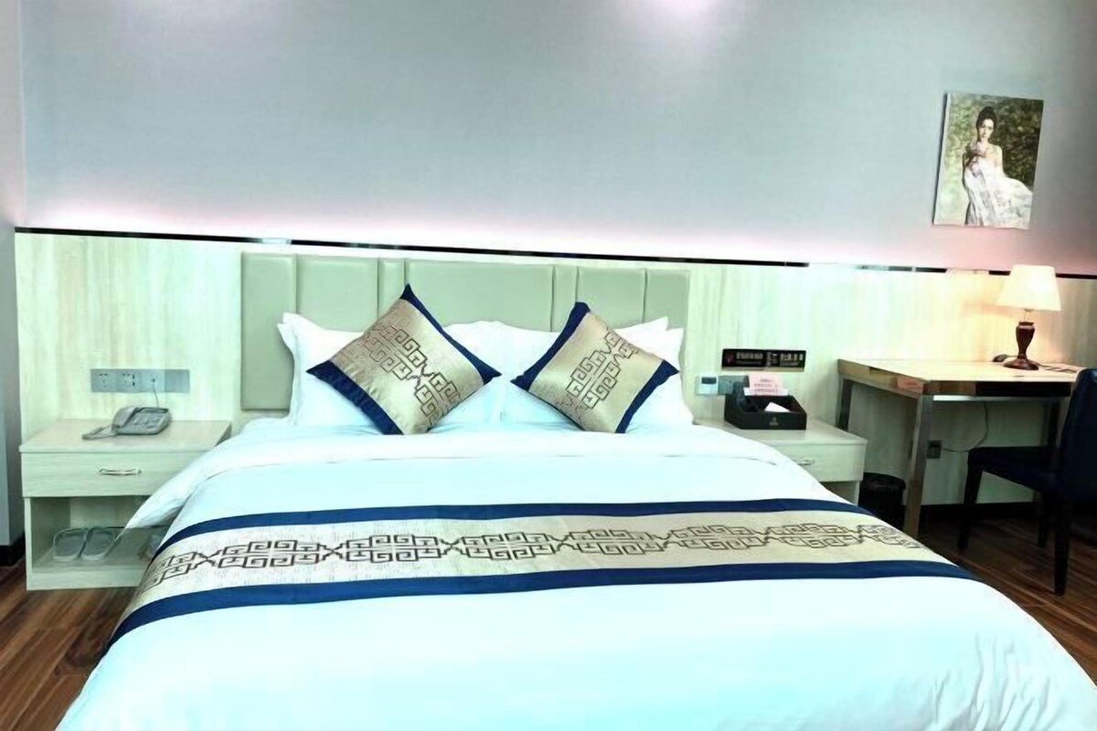 A hotel room with a bed, two pillows, a nightstand, a desk, and a chair.