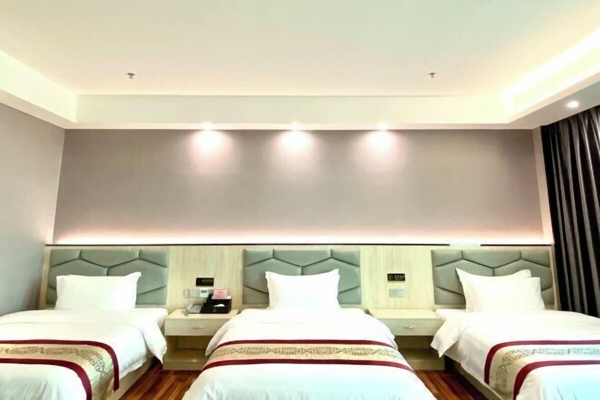 A hotel room with three beds, each with a headboard and bedside tables.