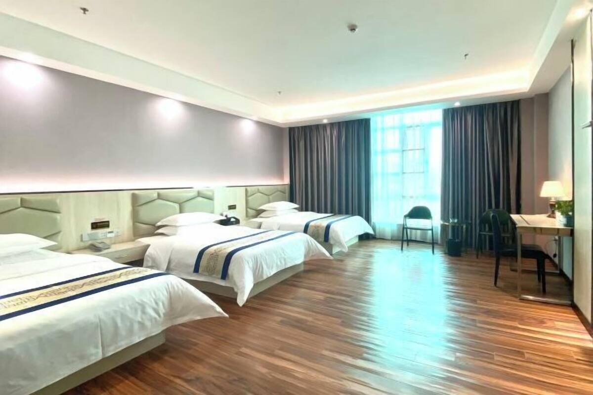 A hotel room with three beds, a desk, and a chair.