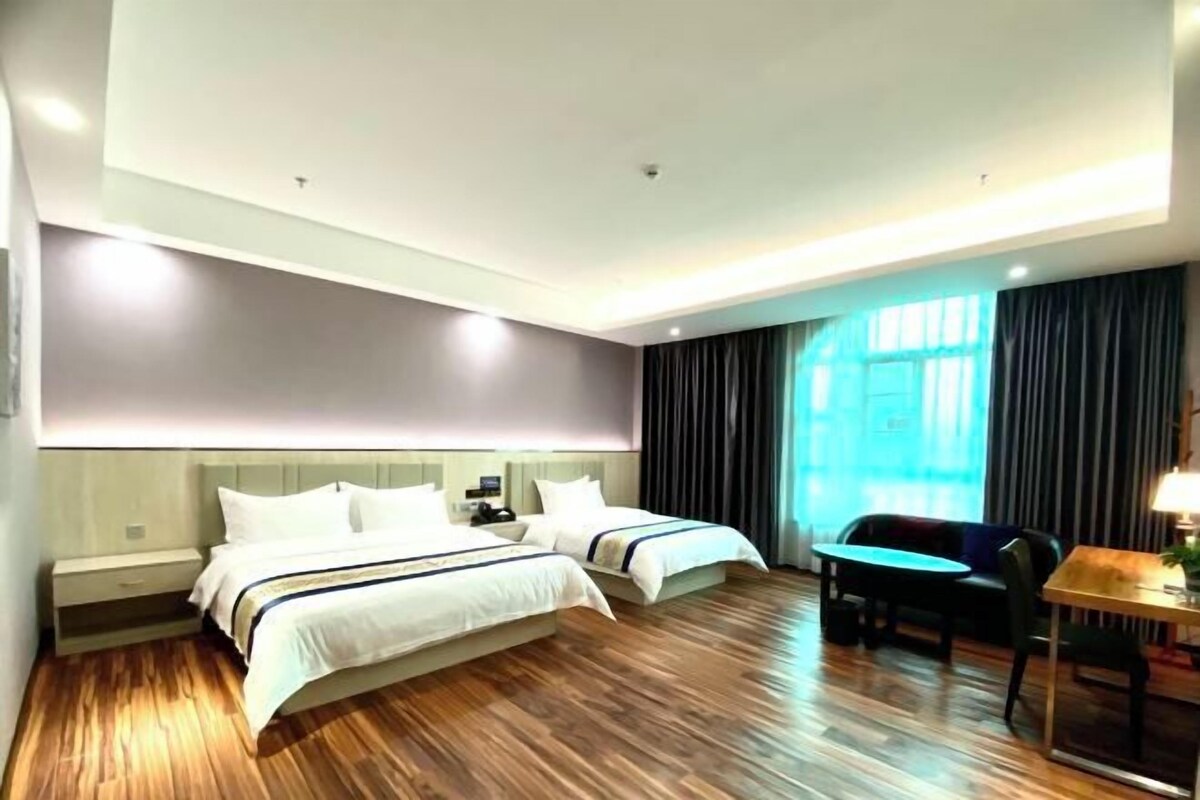 A hotel room with two beds, a desk, a chair, and a large window with curtains.