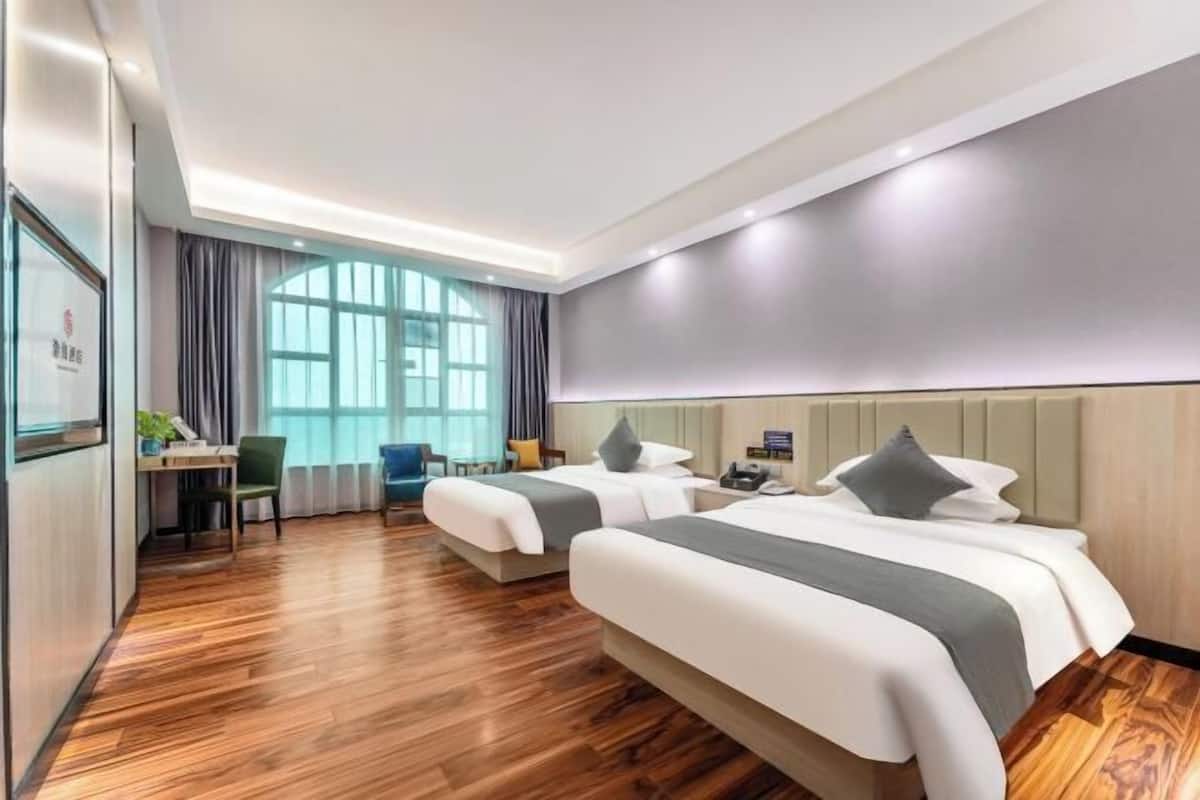 A hotel room with two beds, a desk, a chair, and a large window.
