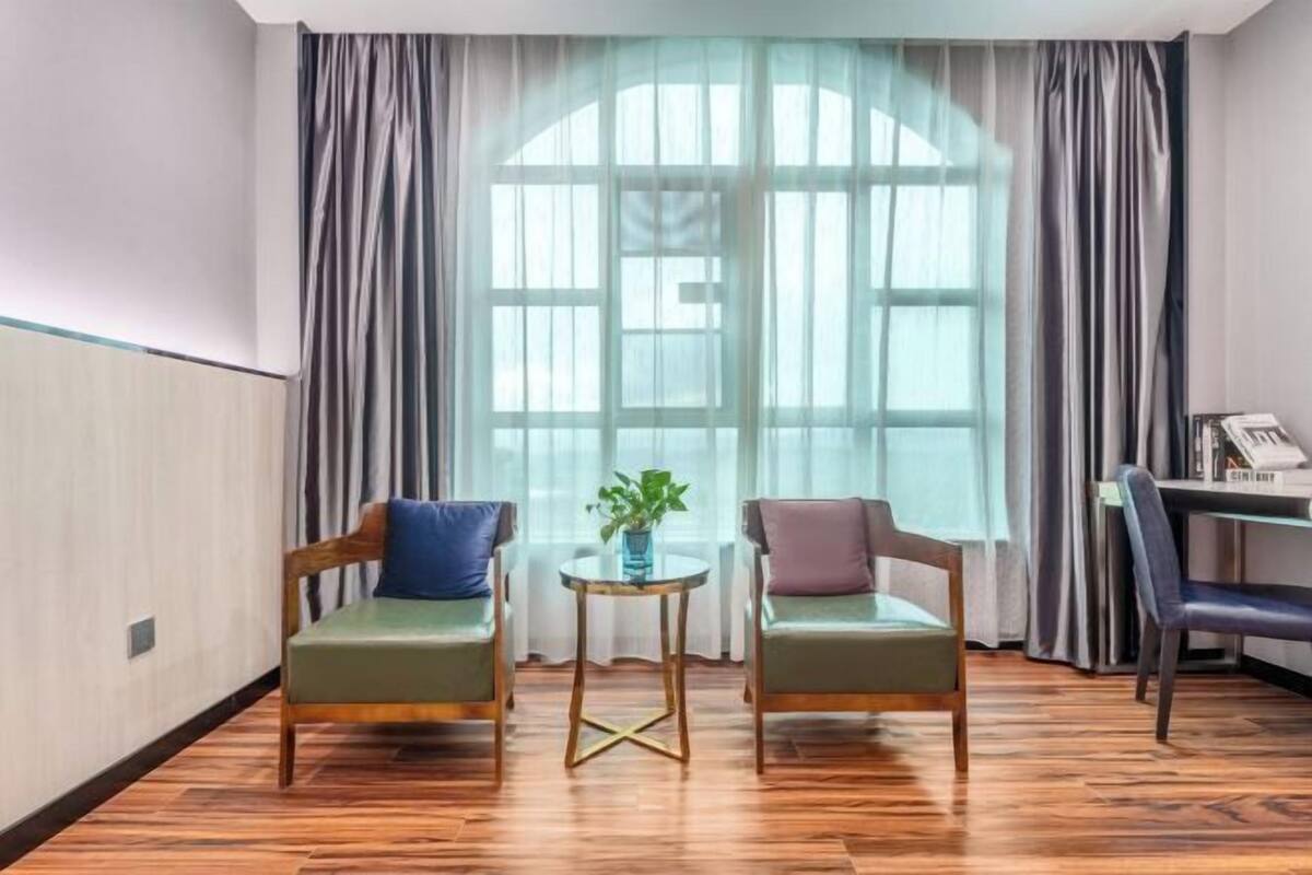 A room with two green sofas, a small round table with a plant, and a large window with curtains.