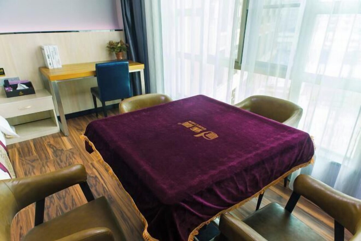 A room with a wooden floor, a desk with a computer, a chair, and a table covered with a purple cloth.