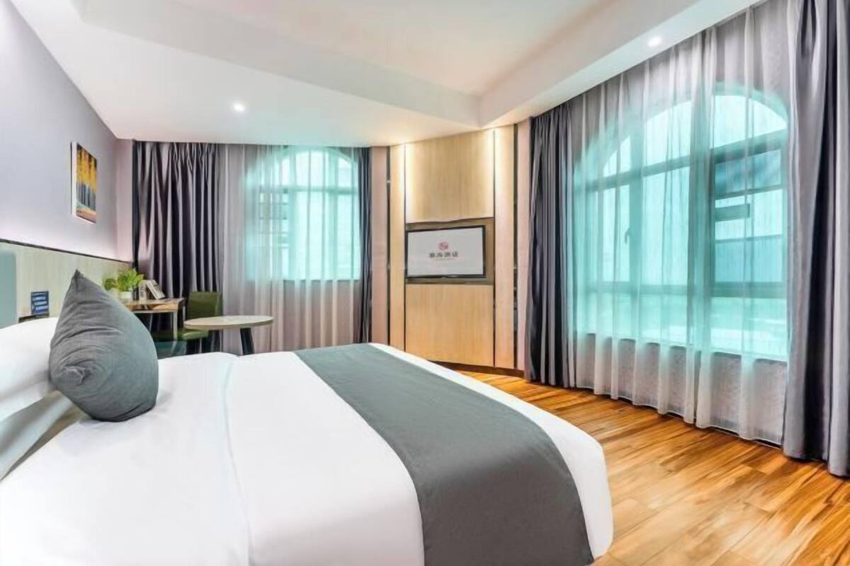 A hotel room with a bed, a desk, and large windows with curtains.