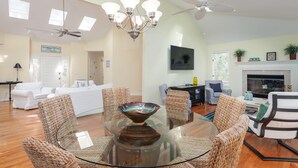 A spacious living room with a glass-top coffee table surrounded by woven chairs, a fireplace, a television, and a ceiling fan. - 3 BR/2BA Home! Screen Porch! Amenity access included! (Seabrook Island)