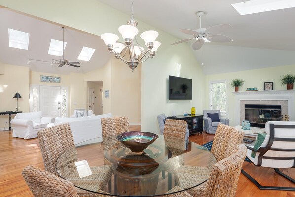 A spacious living room with a glass-top coffee table surrounded by woven chairs, a fireplace, a television, and a ceiling fan. - 3 BR/2BA Home! Screen Porch! Amenity access included! (Seabrook Island)