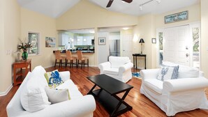 A spacious living room with a high ceiling and a ceiling fan, a kitchen with white cabinets, and a dining area with chairs. - 3 BR/2BA Home! Screen Porch! Amenity access included! (Seabrook Island)