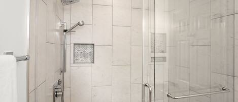 Een moderne douche met een glazen deur, een handdouche en een handmatige kraan.