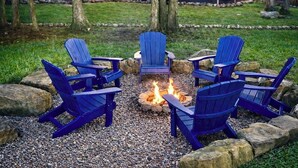 Ein Feuerkorb, umgeben von vier blauen Adirondack-Stühlen in einem Garten.