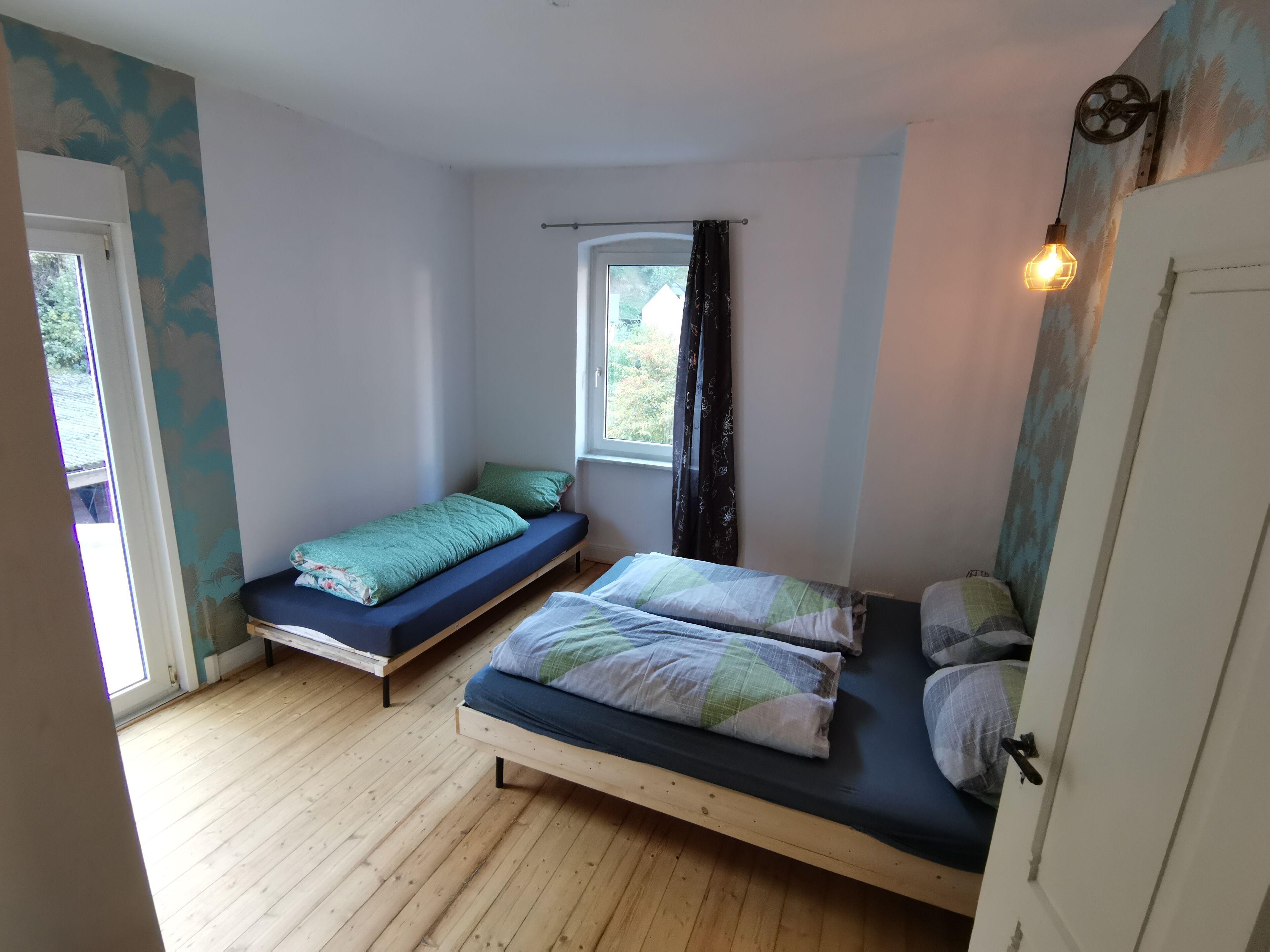 A small, cozy bedroom with two beds, wooden flooring, and a window with curtains.