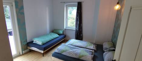 A small, cozy bedroom with two beds, wooden flooring, and a window with curtains.