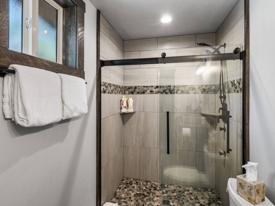 Un baño moderno con ducha de vidrio, inodoro con caja de pañuelos y toallero.