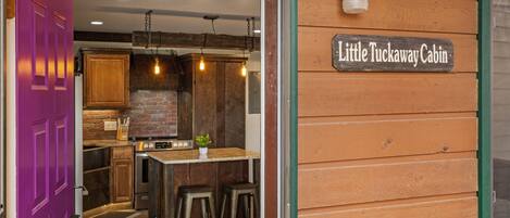 A kitchen with wooden cabinets, a brick wall, and a sign reading "Little Tuckaway Cabin."