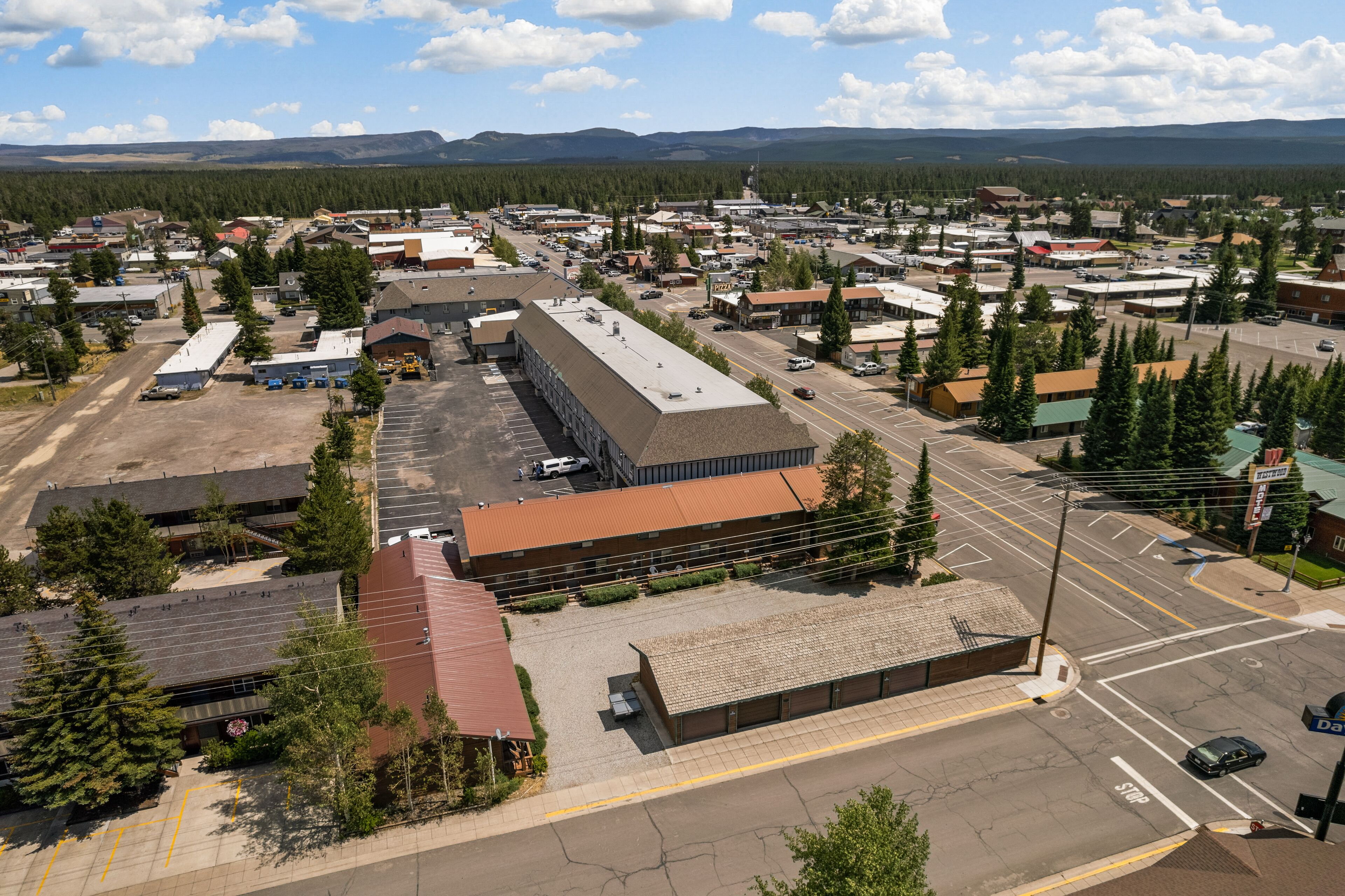 An aerial view of a town with a mix of commercial and residential buildings, a parking lot, and a road intersection.