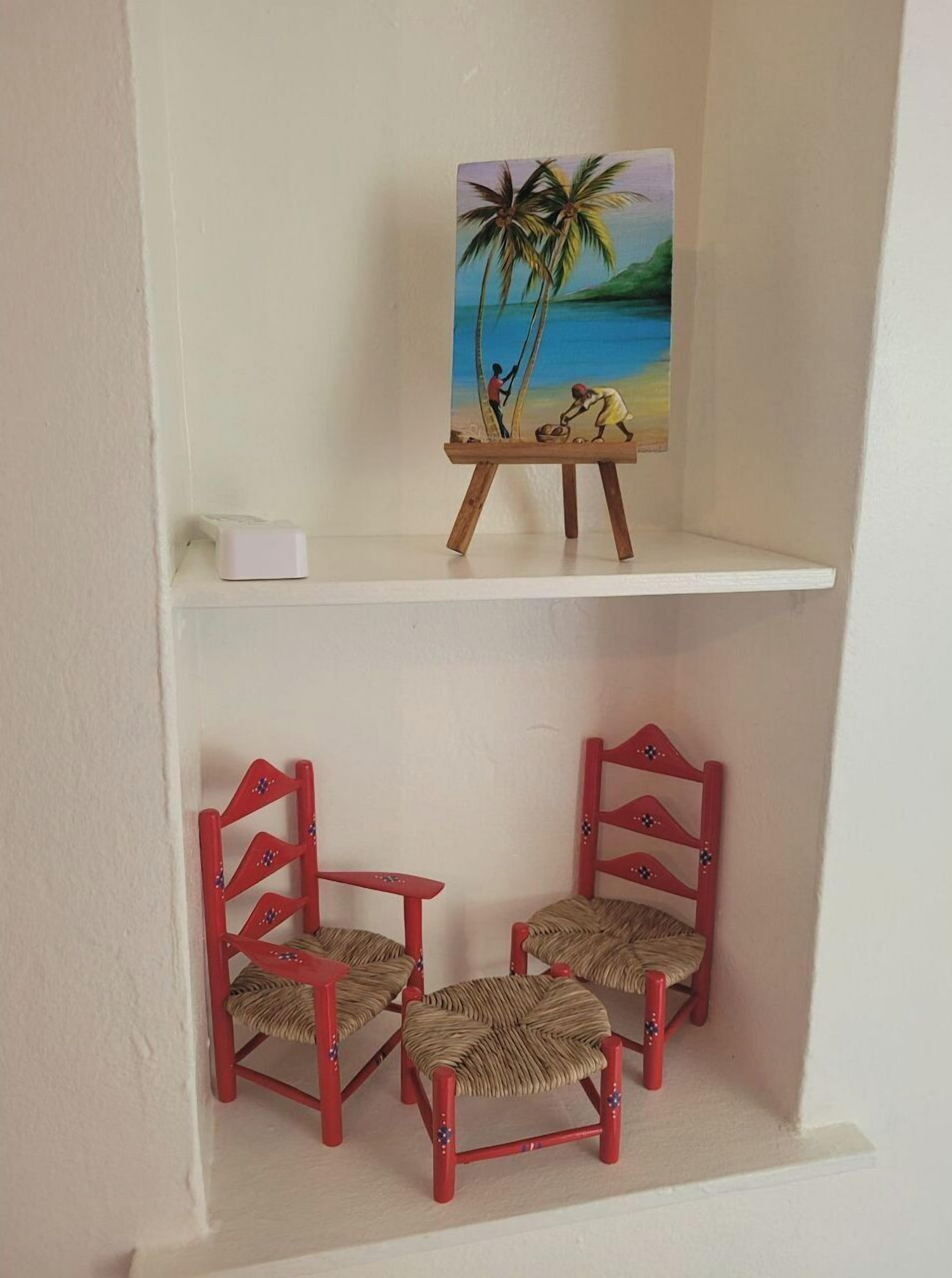 Une étagère sur laquelle est posée une peinture représentant une scène de plage, ainsi que trois chaises rouges à assise tressée.