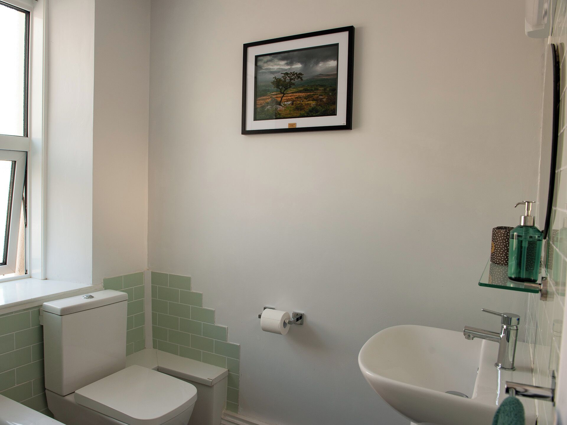 A bathroom with a toilet, sink, and framed picture on the wall.