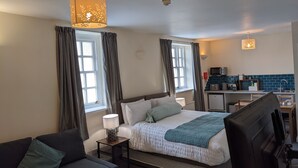 Ein modernes Hotelzimmer mit einem großen Bett, einem Schreibtisch, einem Sessel, einer Lampe und einer Küchenzeile.