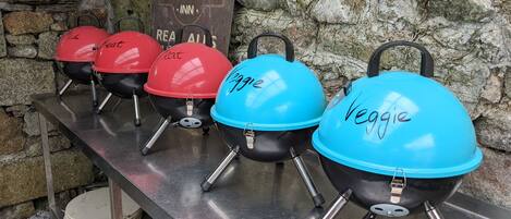 En række grill med skilte der siger "Kød" og "Grønt" foran en stenvæg.