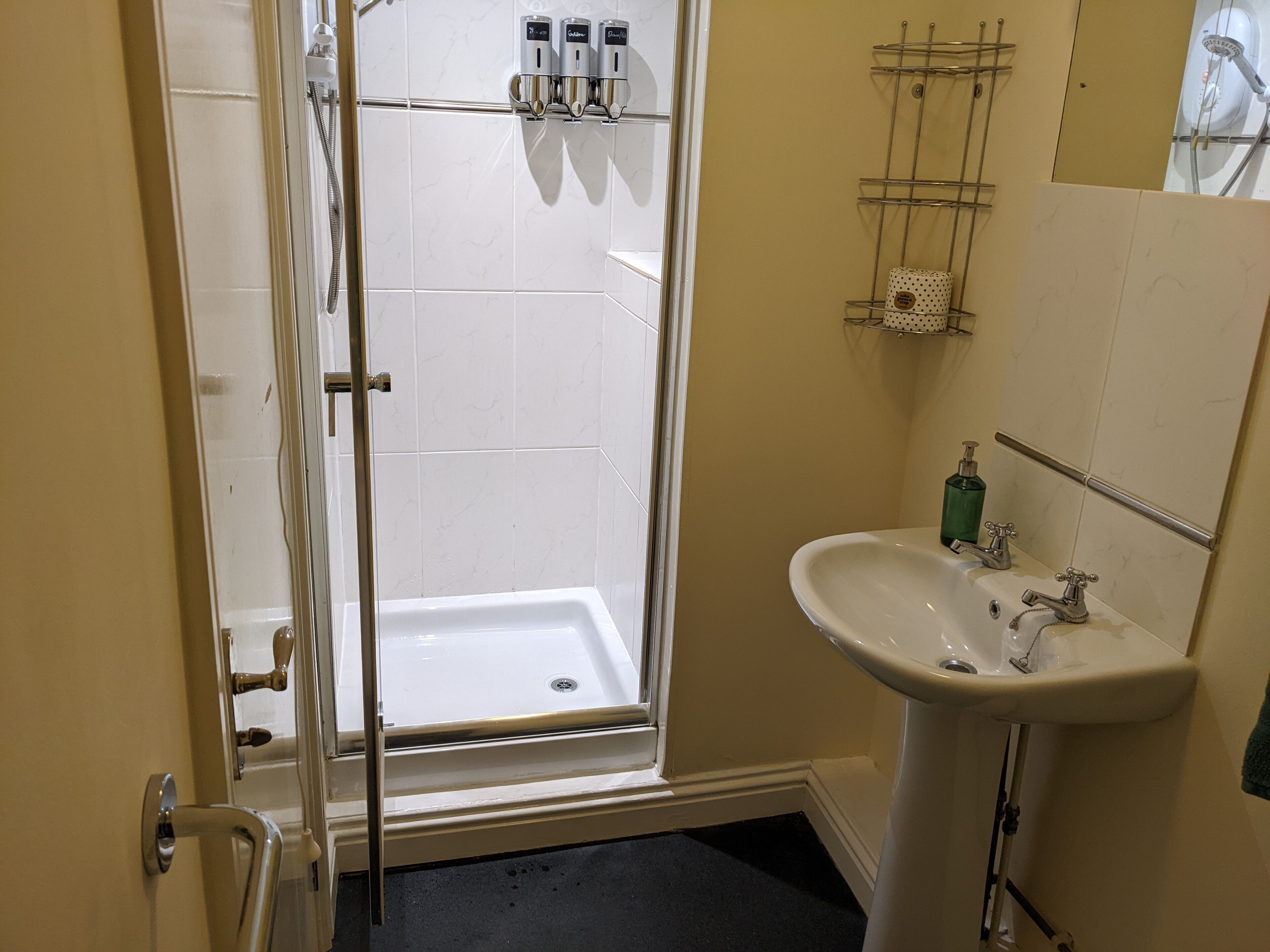 A bathroom with a glass-enclosed shower, a white sink with a soap dispenser, and a towel rack.