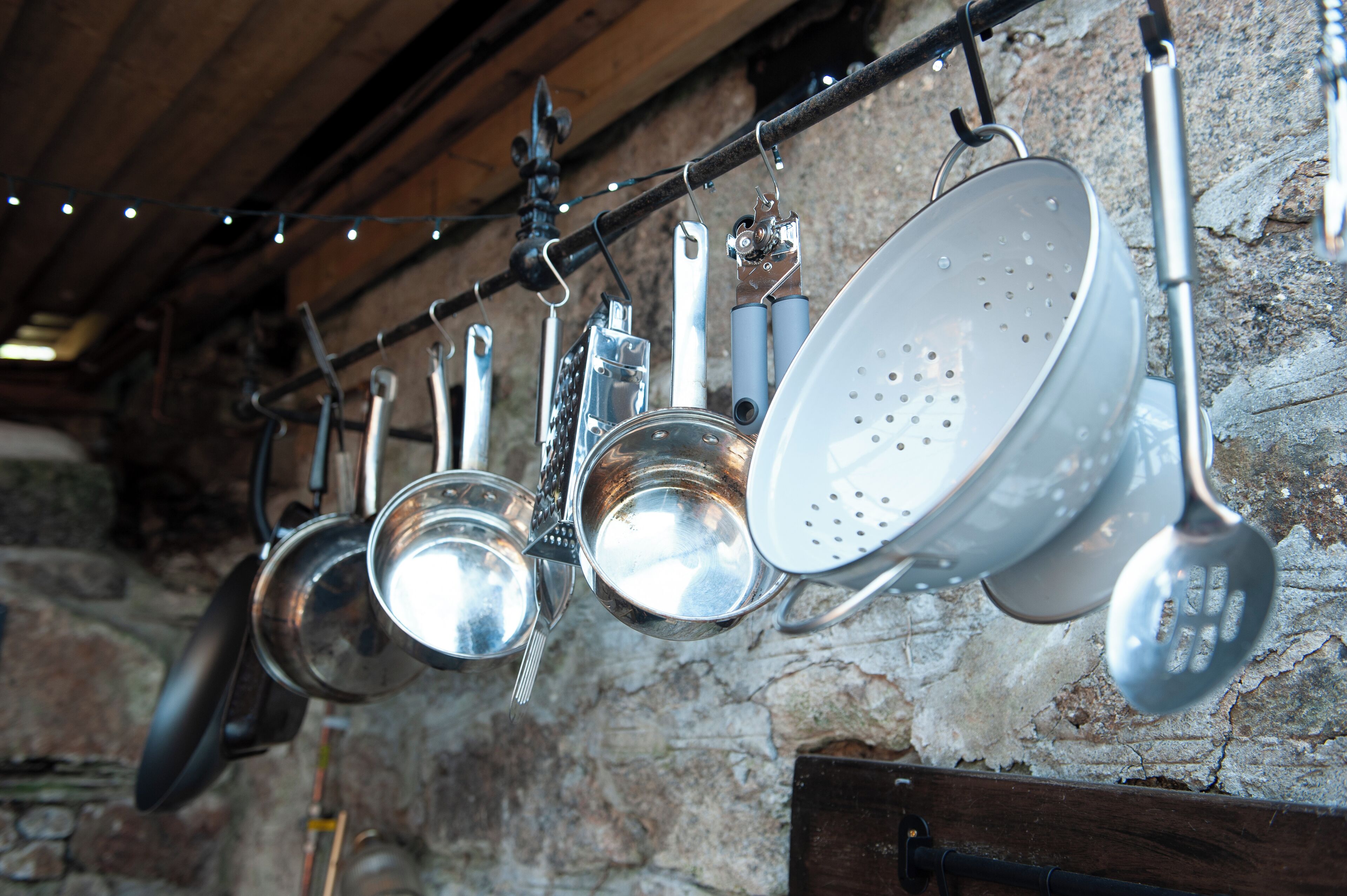 A kitchen with hanging pots and pans on a rack against a stone wall.
