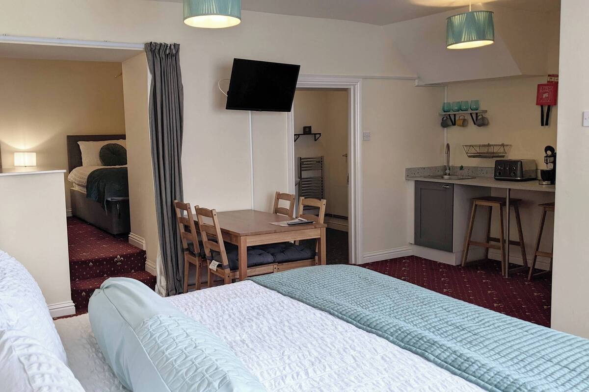 A compact hotel room with a bed, a desk, and a kitchenette.