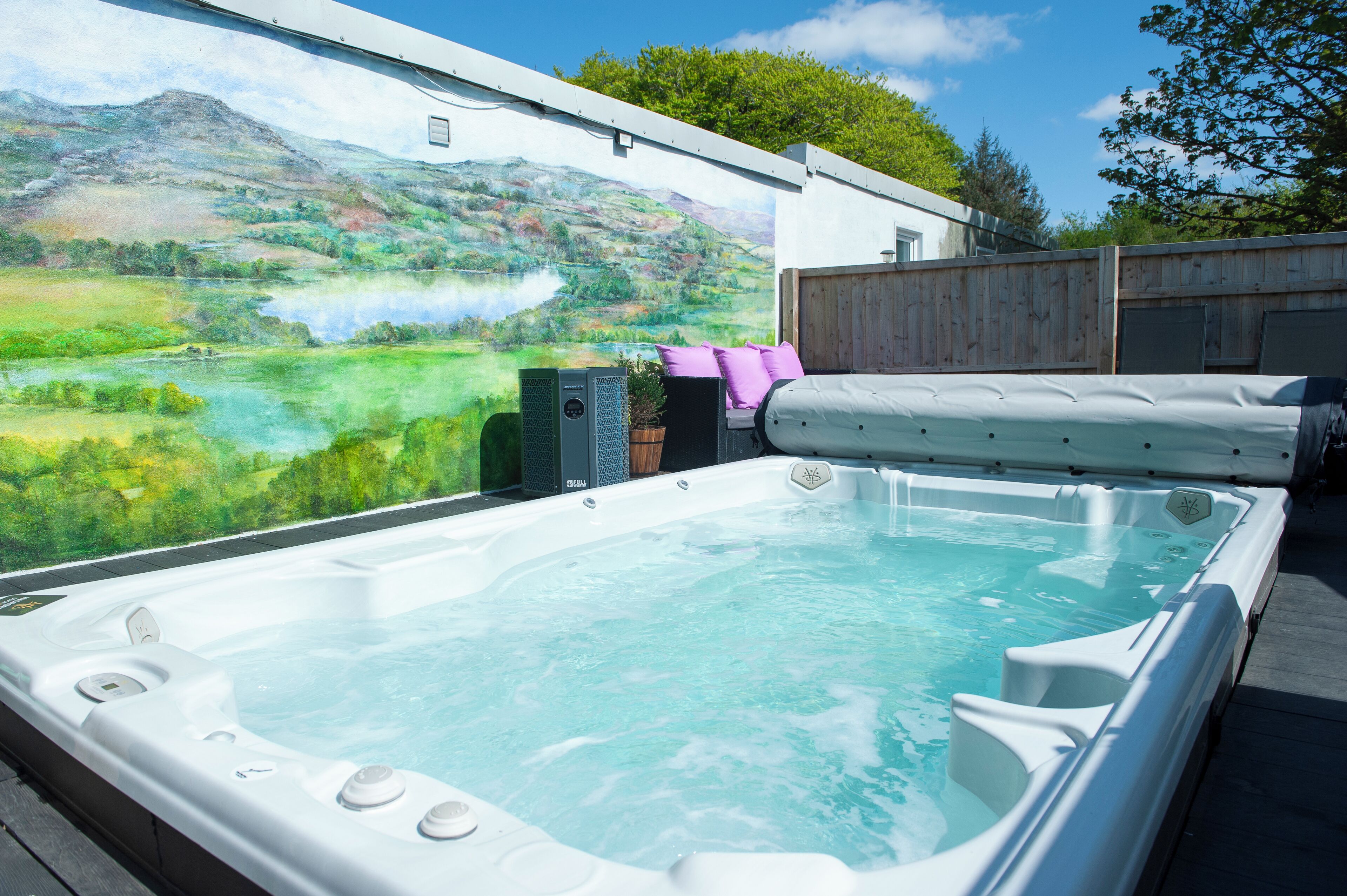 Un jacuzzi con un mural panorámico de fondo, una terraza de madera y una valla de madera.