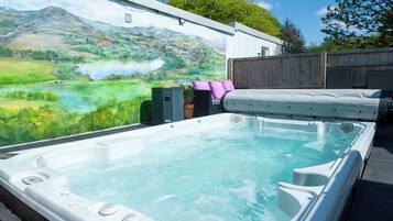 Un jacuzzi con un mural panorámico de fondo, una terraza de madera y una valla de madera.