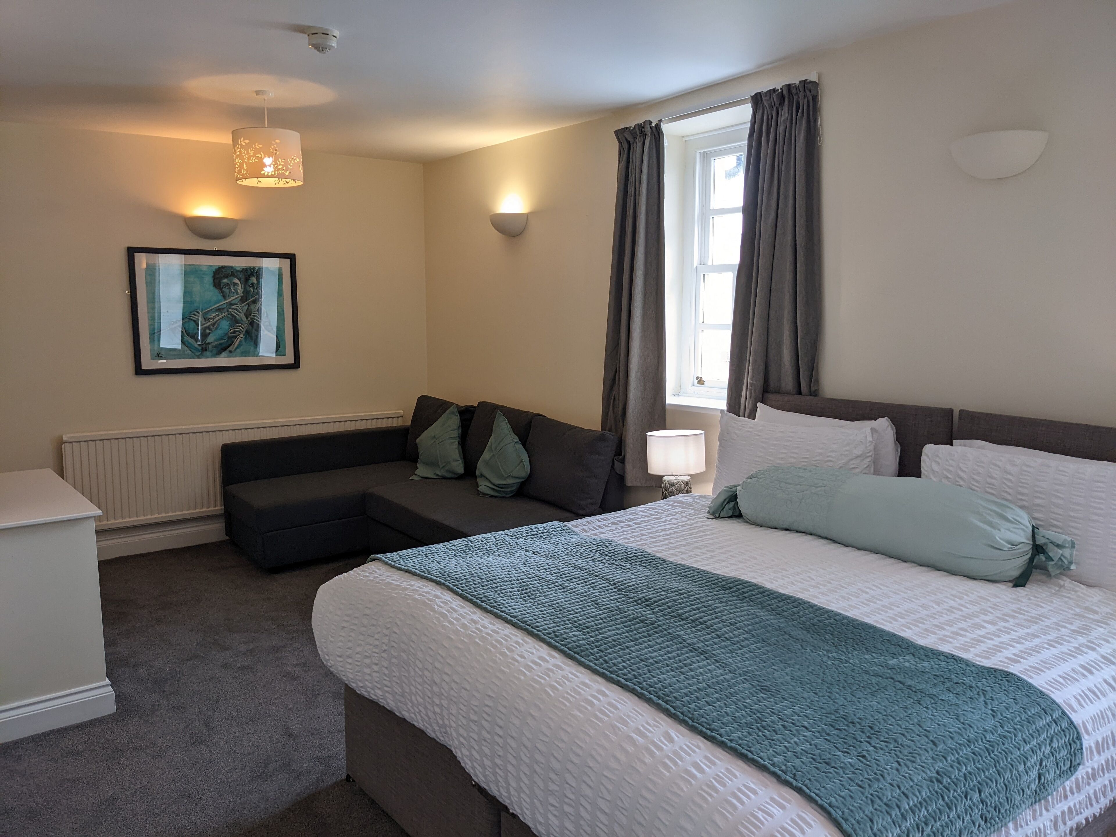 Una habitación de hotel moderna con una cama grande, un sofá, una mesita y un cuadro en la pared.
