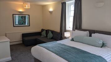 Una habitación de hotel moderna con una cama grande, un sofá, una mesita y un cuadro en la pared.