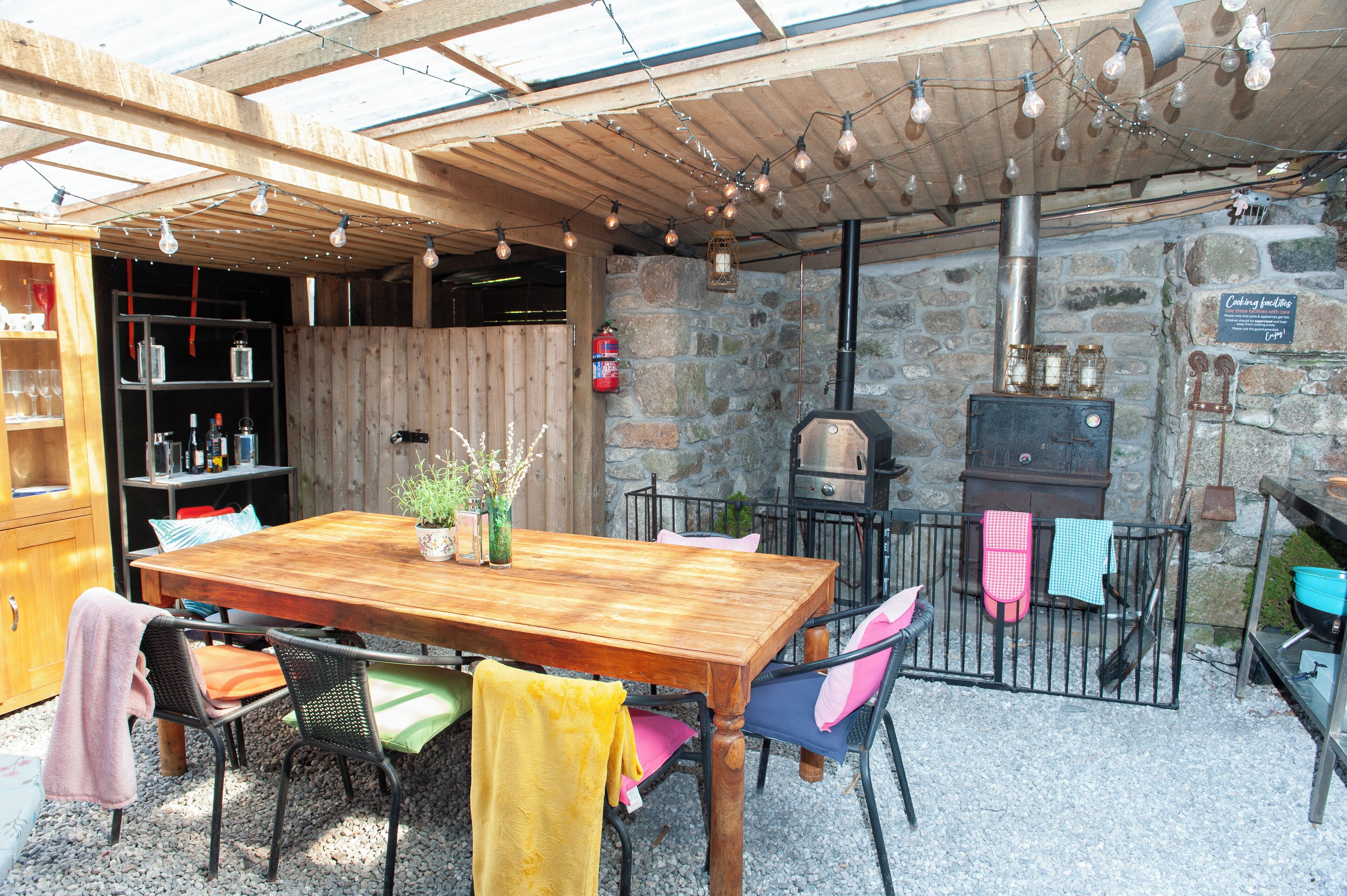 An outdoor patio with a wooden table, chairs, and a stone wall.