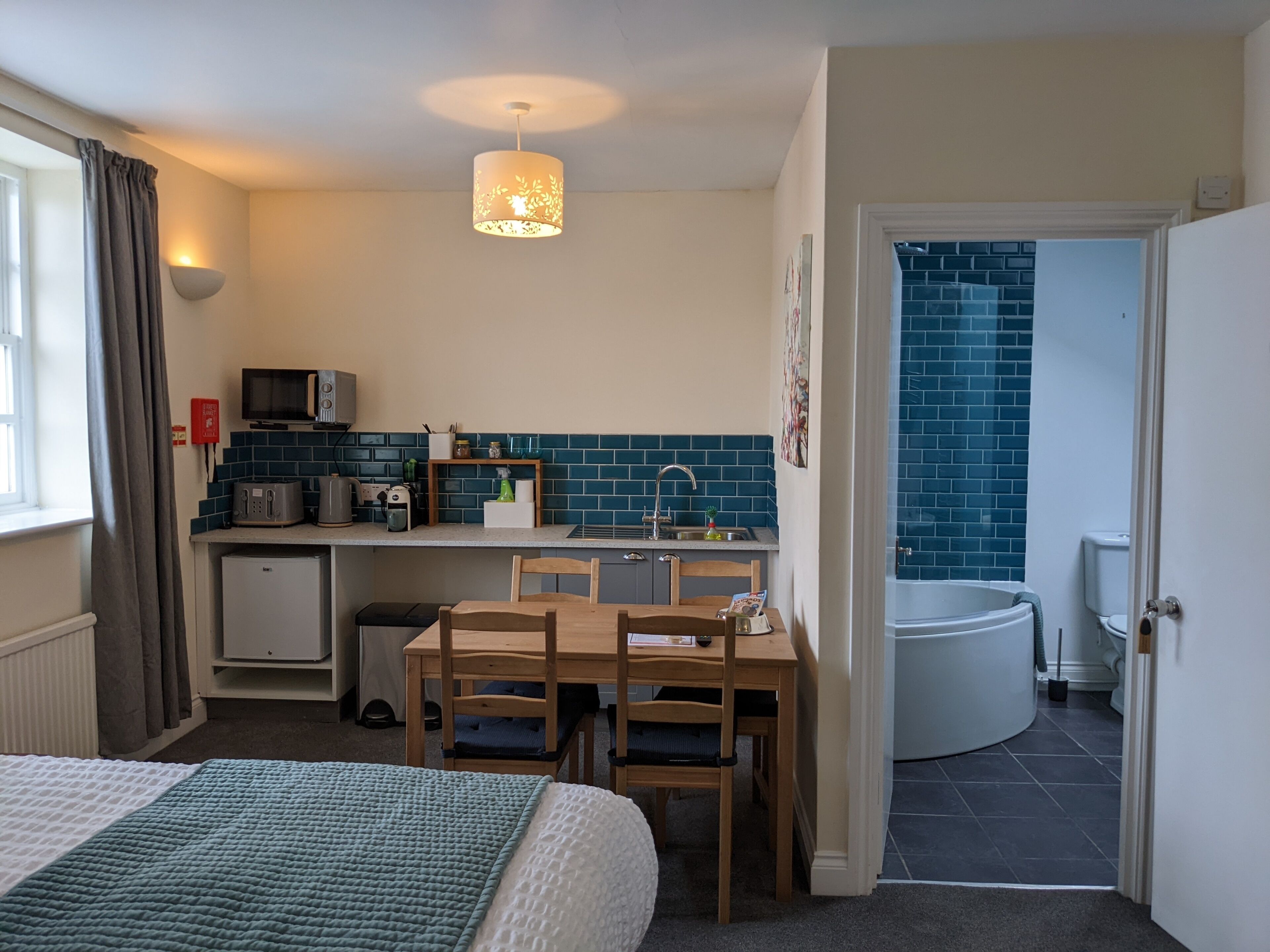 A compact room with a bed, a small kitchenette, a dining area, and a bathroom.