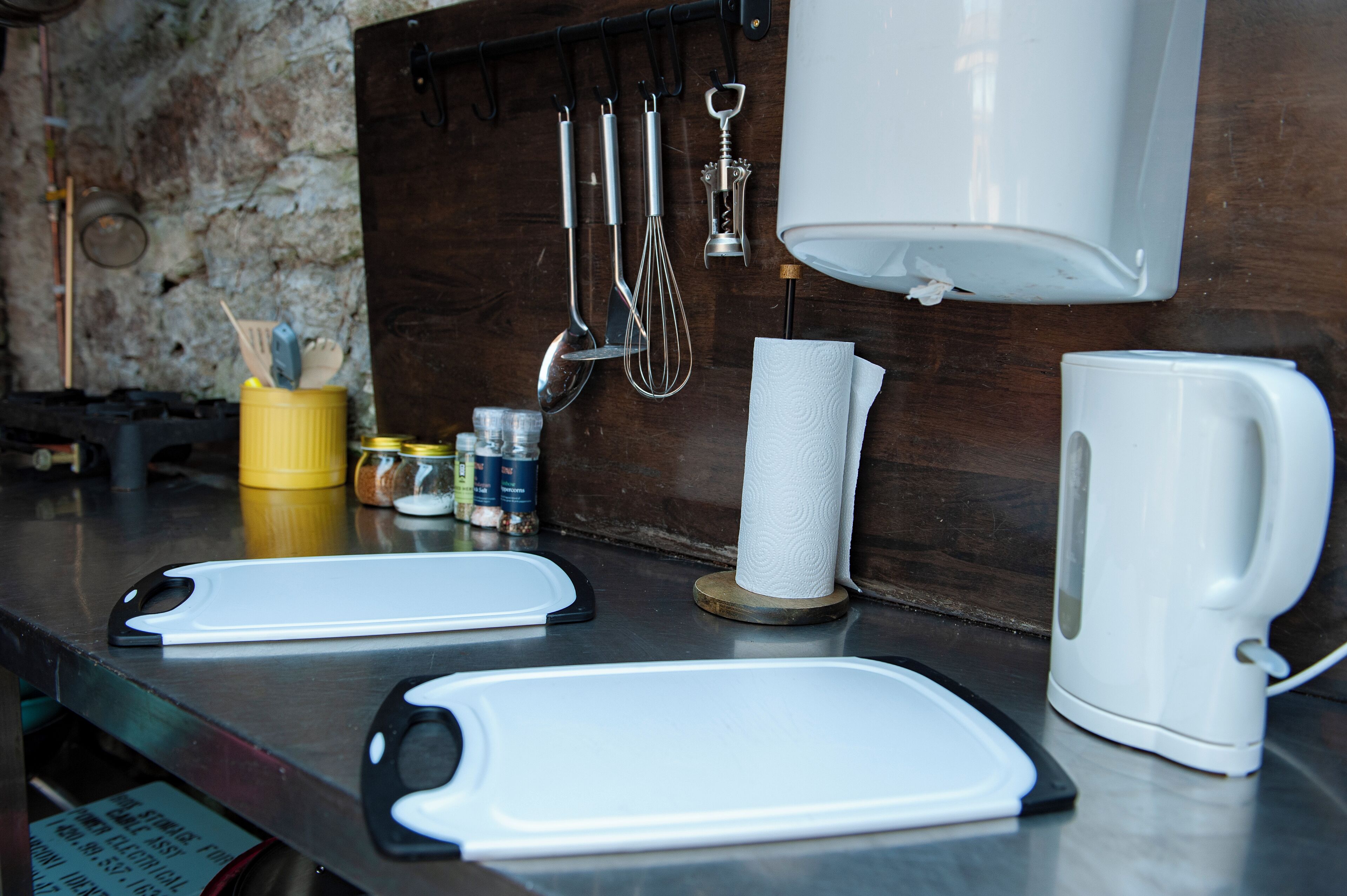 A kitchen counter with a coffee maker, cutting boards, a paper towel holder, and various utensils.