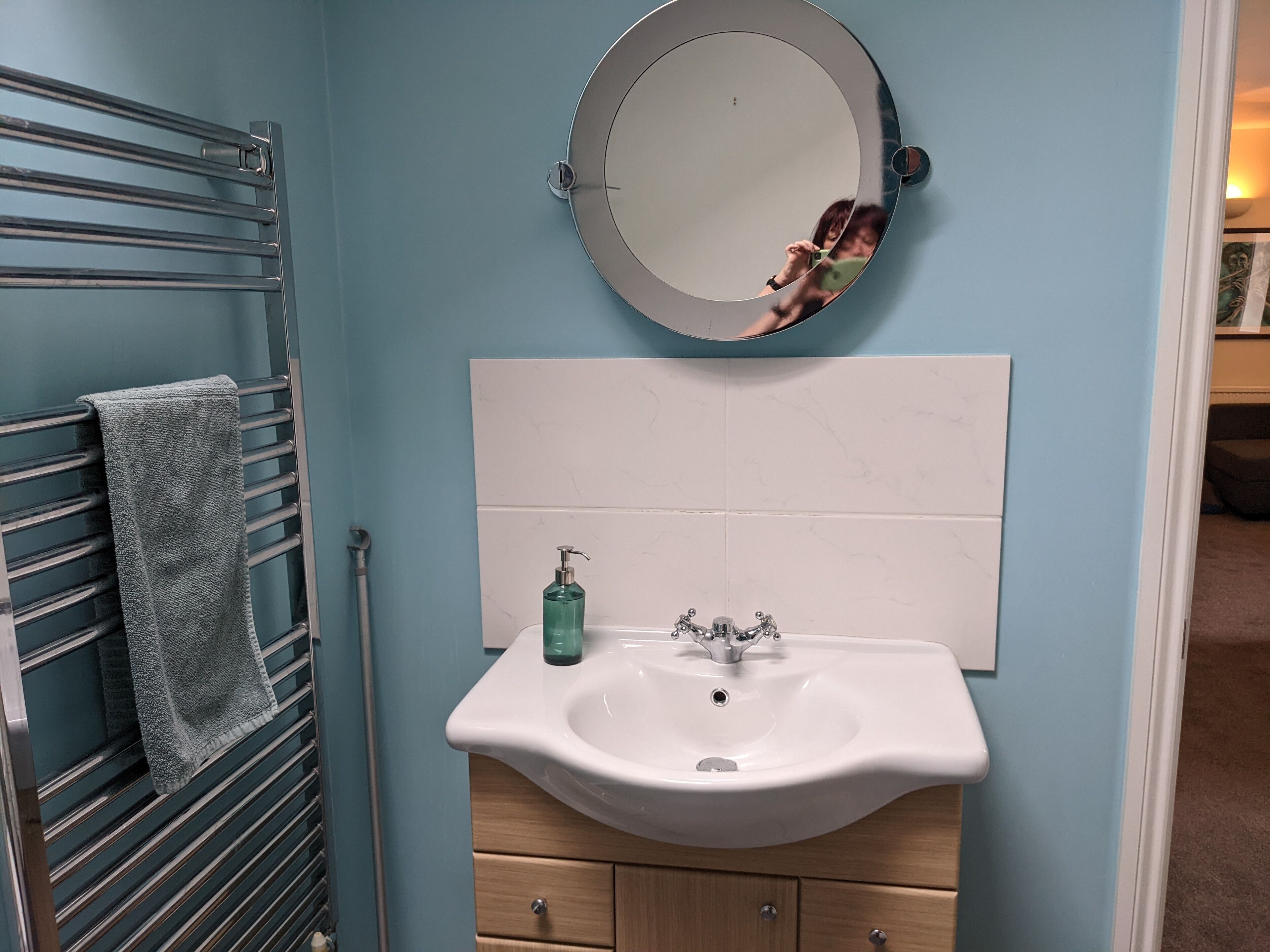 Een badkamer met een handdoekhouder, een wastafel met een zeepdispenser en een spiegel.