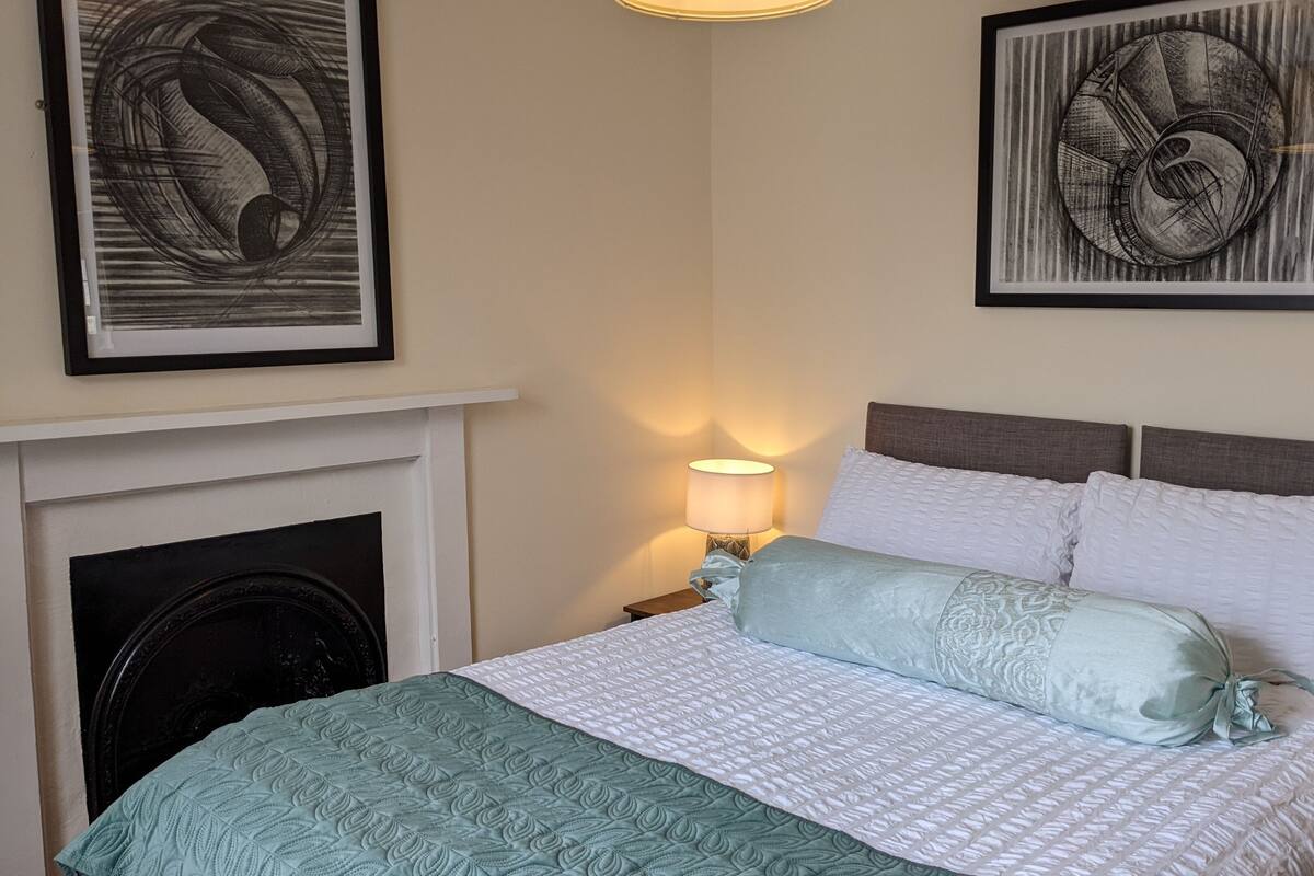 A neatly arranged bedroom with a bed, a nightstand, a lamp, and a fireplace.