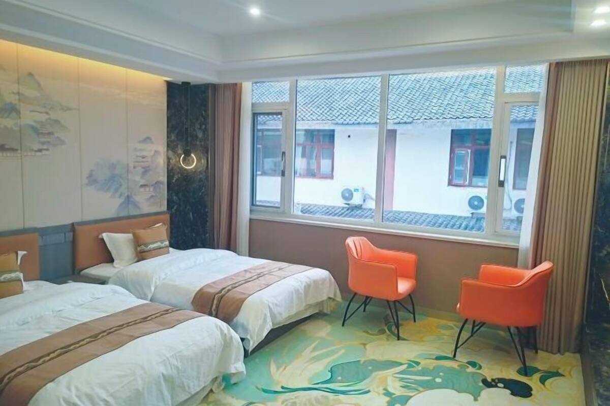 Ett hotellrum med två sängar, ett fönster med utsikt över byggnader och en dekorativ vägg.