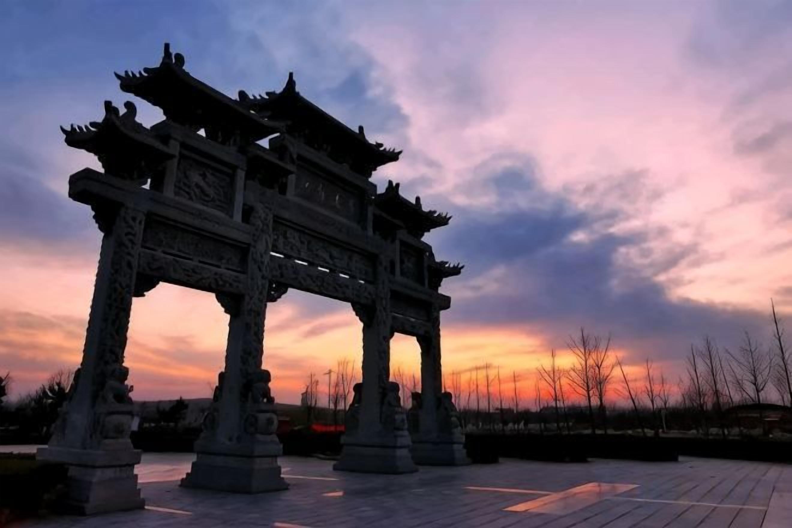 A traditional gate structure with intricate carvings, set against a twilight sky.