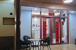 A hotel entrance with a reception desk, a glass door with a red sign, and a small seating area with chairs and a table. - Pingyi to This Inn Travel Inn (Pingyi)