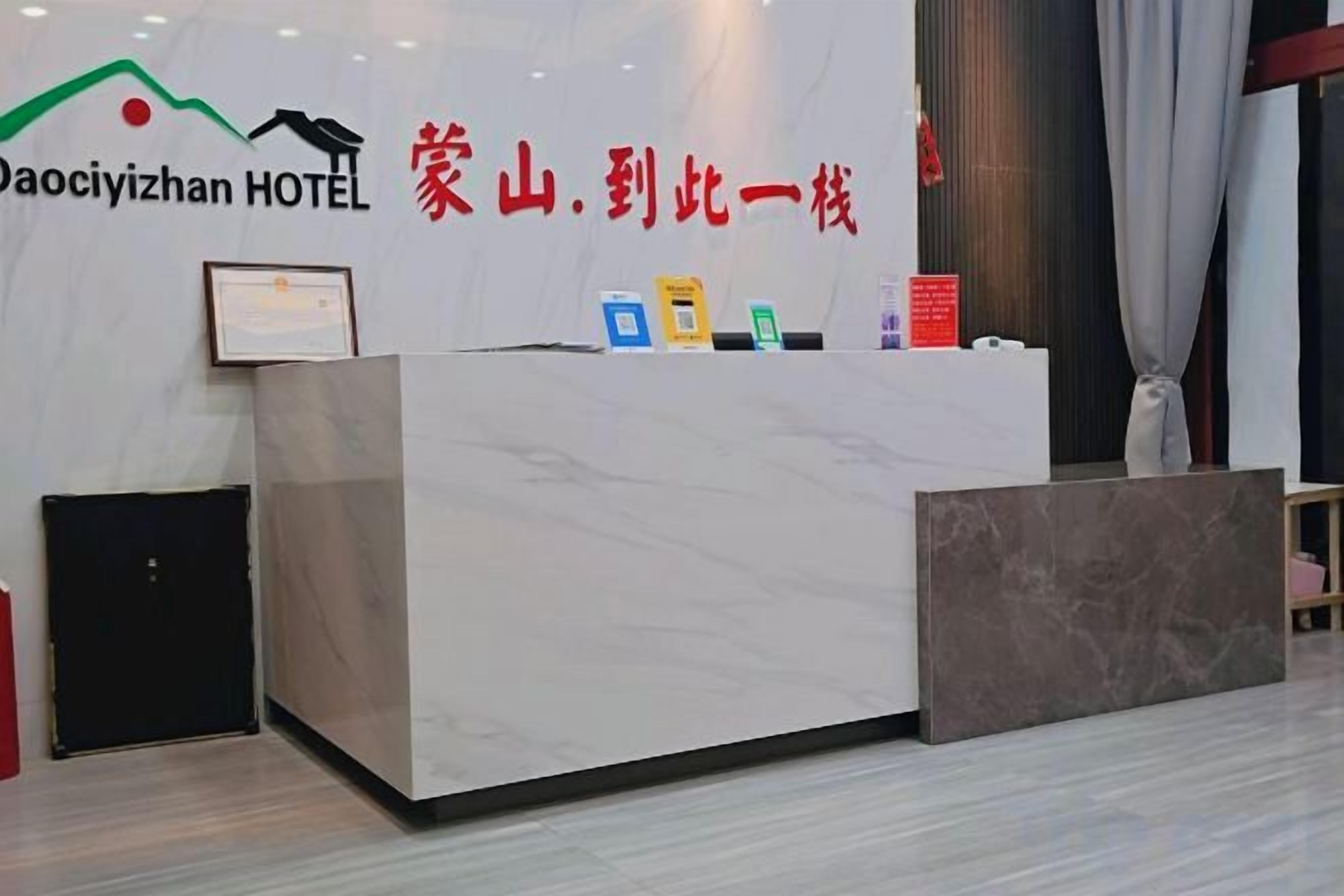 A hotel reception desk with a marble counter, a framed certificate, and a sign with hotel name and slogan.