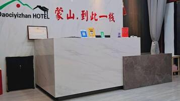 Ein Hotelrezeptionsschalter mit einer Marmorplatte, einem gerahmten Zertifikat und einem Schild mit dem Hotelnamen und dem Slogan.