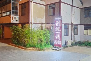 Um edifício com uma placa em idioma estrangeiro, fachada de tijolos e uma pequena área ajardinada.