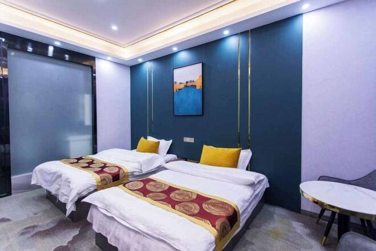 A hotel room with two beds, a small table, and a painting on the wall.