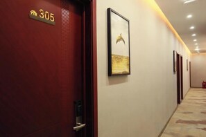 A hotel corridor with a red door marked '305', a framed picture on the wall, and a carpeted floor. - Pingyi to This Inn Travel Inn (Pingyi)