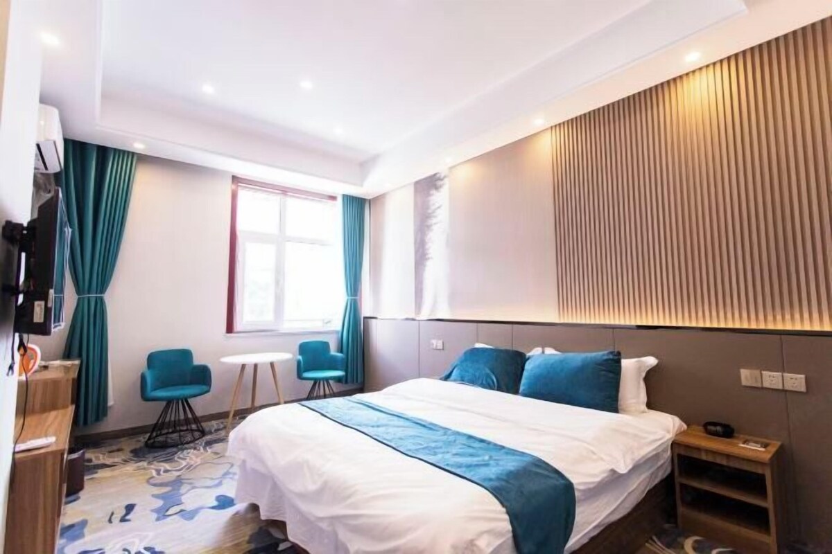 A modern hotel room with a large bed, a desk, a chair, and a TV.
