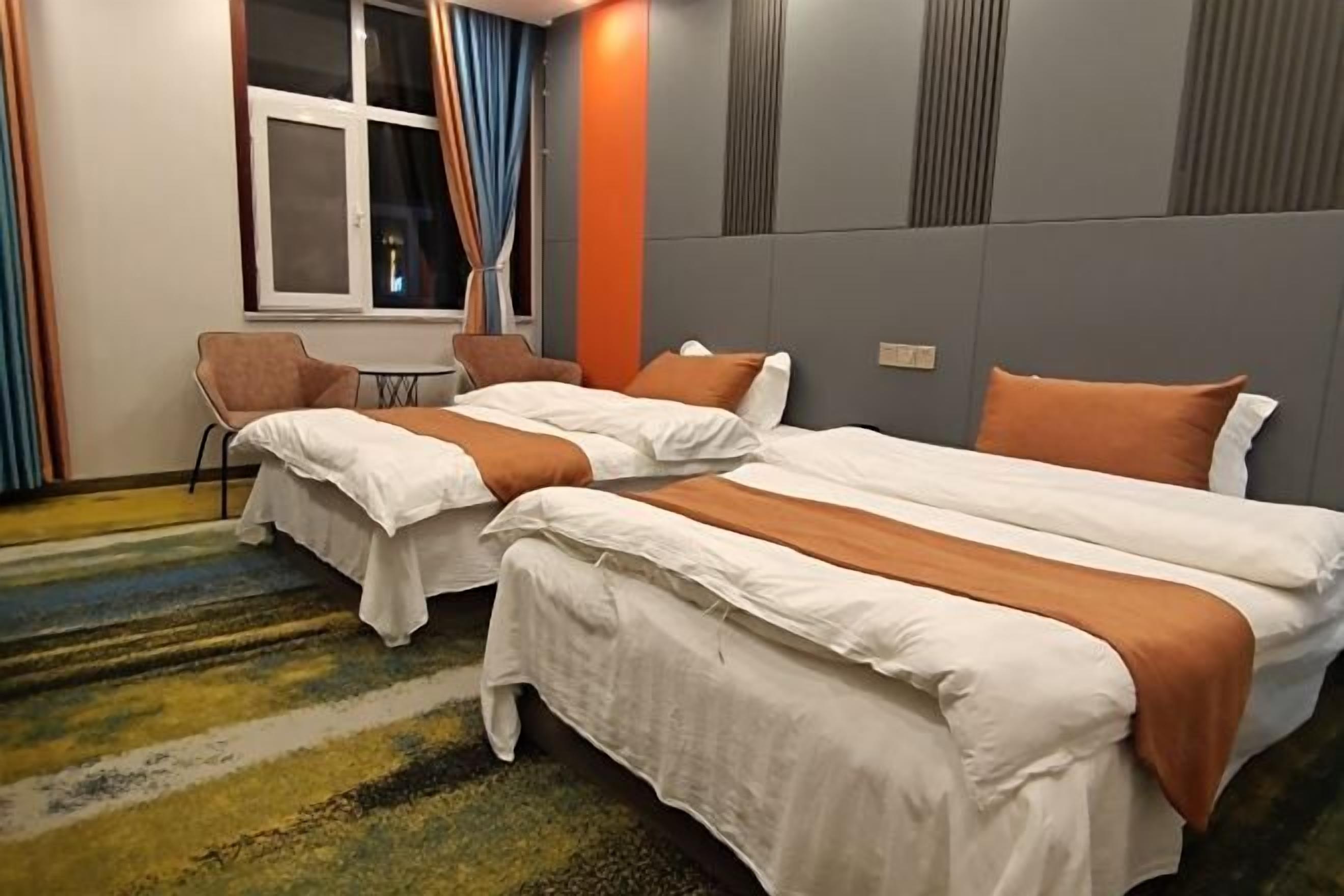 Une chambre d’hôtel avec deux lits, une fenêtre avec des rideaux, une petite table et une chaise.